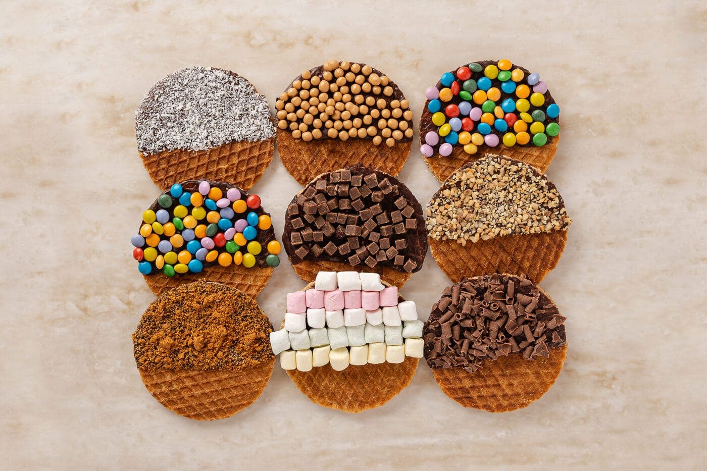 An overhead spread of decorated stroopwafels with chocolate, candy and marshmallow toppings