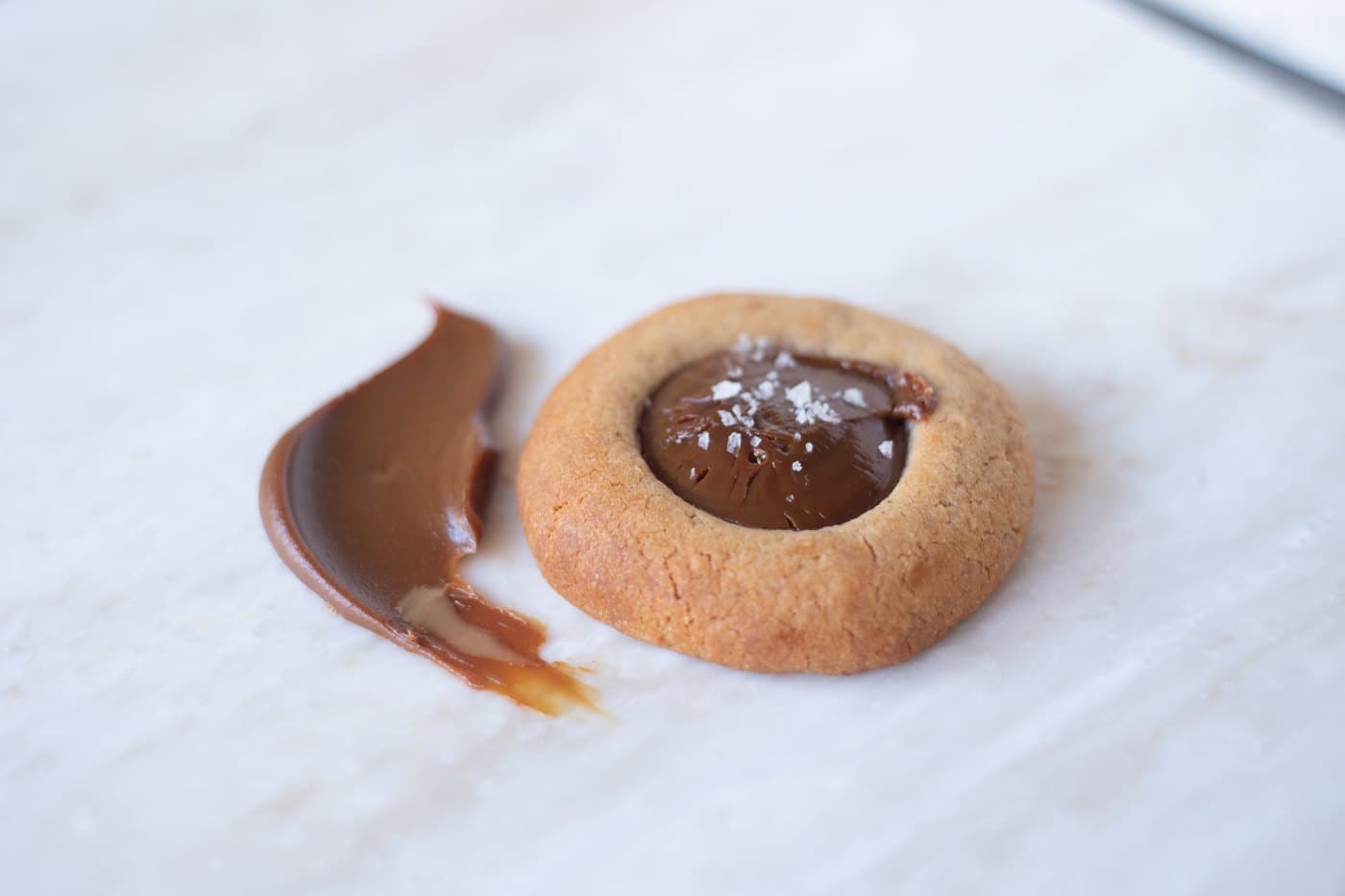 Dikke zelfgemaakte dulce de leche op marmer, naast een gevuld koekje